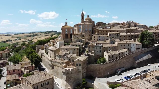 Cinematic aerial view of Corinaldo, Italy, captured by drone on a bright sunny day. Panoramic footage of the well-preserved medieval town, stone buildings, and rolling hills of the Marche countryside.