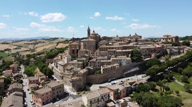 Aerial drone footage of Corinaldo, Italy, a historic hilltop town in the Marche region. Sunny daytime view of medieval walls, rooftops, and surrounding countryside, showcasing traditional Italian arch