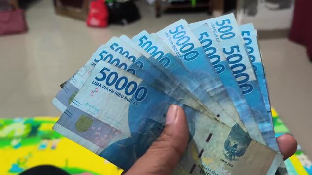 An adult's fingers holding an Indonesian fifty thousand rupiah banknote