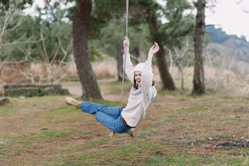 Obraz premium Woman on a swing in an outdoor park, carefree moment, smiling and enjoying fresh air, nature around, casual outfit, playful balance, rustic setting, serene afternoon, light breeze, candid lifestyle