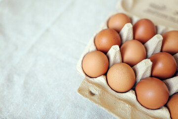 Fresh eggs are arranged neatly in a cardboard carton on a cloth surface in a kitchen