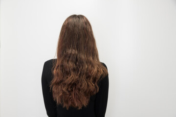 Naklejka premium A rear studio shot capturing a woman with long, wavy hair against a plain white background. This image serves as a before shot, showcasing the current state and texture of the hair 