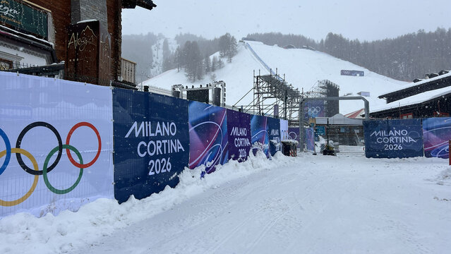 Livigno, Italy - February 4, 2026: Snowy access road and temporary fencing with Milano Cortina 2026 Winter Olympics branding at the Livigno freestyle and snowboard venue during heavy snowfall