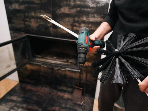 Man preparing to clean a modern indoor fireplace with a professional chimney brush.