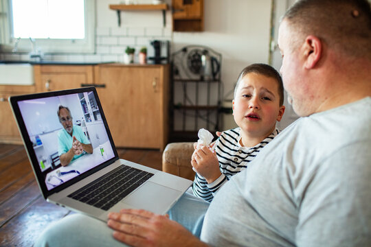 Father comforting sick son during online doctor video call at home