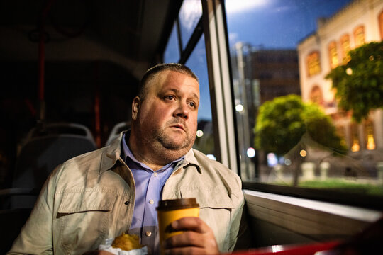 Middle-aged man commuting on night bus with coffee