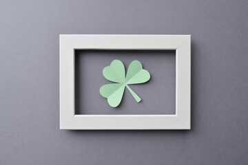 Paper three-leaf clover in a white wooden frame on a gray background