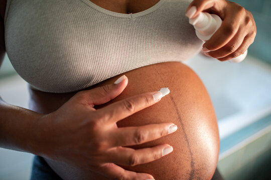 Pregnant woman applying belly lotion in bathroom