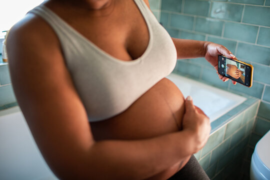 Expectant mother taking belly selfie in bathroom