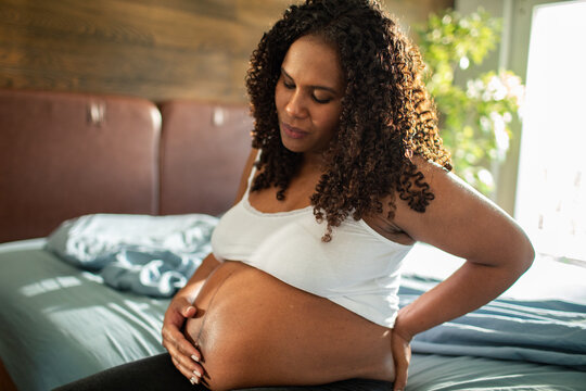 Pregnant woman with backache holding belly in bedroom