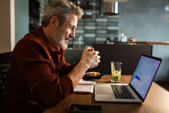 Senior man working on laptop at home kitchen table