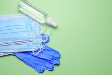 Medical masks, protective gloves and sprayer on green background