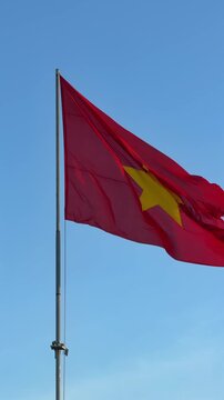 Vertical slow motion shot of Vietnam flag flowing in the wind, glowing softly in sunset rays against open sky behind the flag. Cultural heritage.