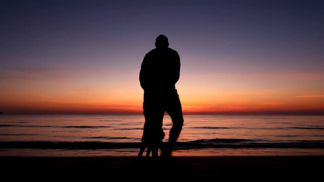 A family, silhouetted against a vibrant sunset sky at the beach, with the parents holding hands of a child. The calm ocean complements the sky's colors