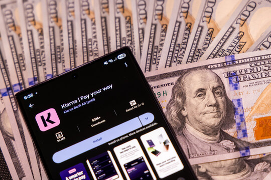 Cellphone with Klarna app in Google play over dollar banknotes - Balykchy, Kyrgyzstan - December 29, 2025
