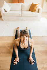 Woman smiling while performing a yoga cobra pose on a mat at home