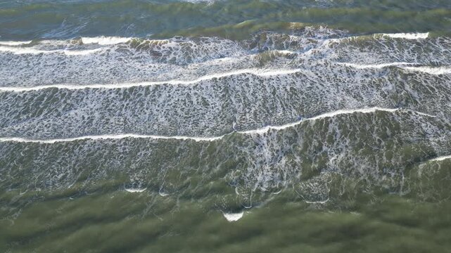 A bird's-eye view of the waves crashing onto a sandy beach - Vue a&eacute;rienne &agrave; la verticale des vagues sur une plage de sable
