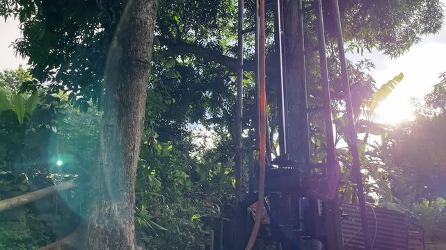 Water well drilling rig surrounded by trees with sunlight flare, creating a hopeful and optimistic atmosphere. The footage highlights human effort, natural resources, and progress toward clean water a