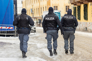Italian Polizia officers patrol a snowy street in Cortina d Ampezzo, framed by Alpine architecture and international flags, reflecting Olympic spirit, winter security, and calm crowd control.