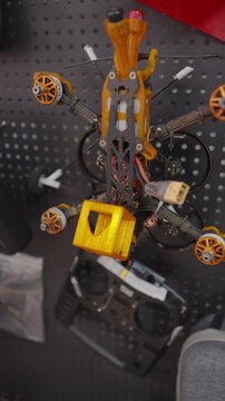 Custom built FPV racing drone with lightweight carbon fiber frame, displayed in workshop environment, quadcopter designed for drone racing and freestyle flying, remote controller visible in background