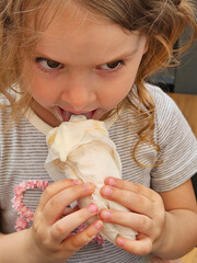 Girl is eating a banana split or ice cream. She is wearing a striped shirt. The banana split is covered in napkins