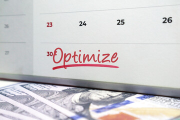 Calendar with the word Optimize handwritten in red ink over US hundred dollar bills. Concept for maximizing financial efficiency, improving investment returns, and refined budget management.