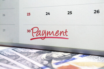 Calendar with the word Payment handwritten in red ink over US hundred dollar bills. Concept for settlement of debts, monthly installments, business transactions, and financial obligations.