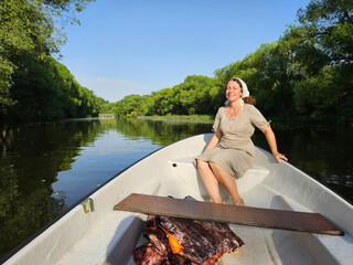 Woman is sitting in a boat on a river. The boat is white and has a brown board on the bottom