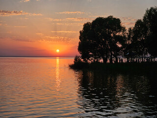 Sunset over a lake with trees in the background. The sun is setting and the sky is orange