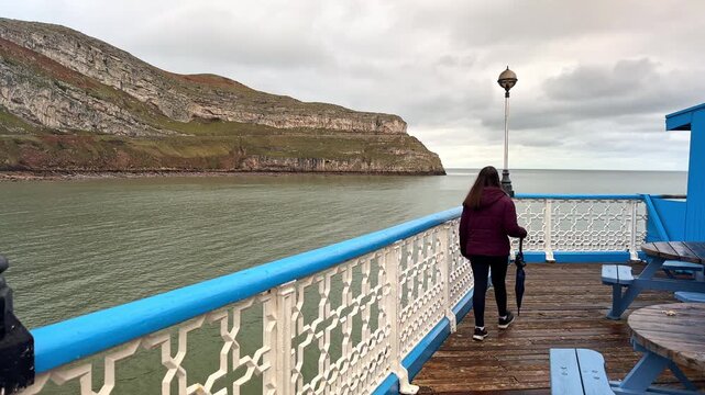 Woman Walking on Llandudno Victorian Pier with View to the Great Orme, Conwy, North Wales, UK
