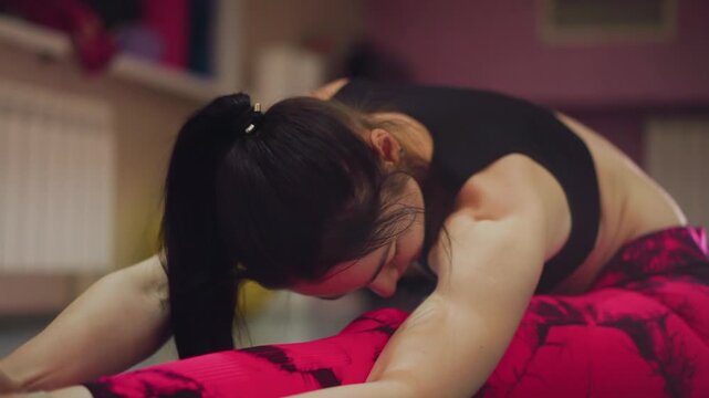 white woman reaching for toes focused, intimate studio hamstring stretch with controlled breathing and slow motion, pink leggings, hands gripping foot, recovery and mindfulness emphasis, sustained