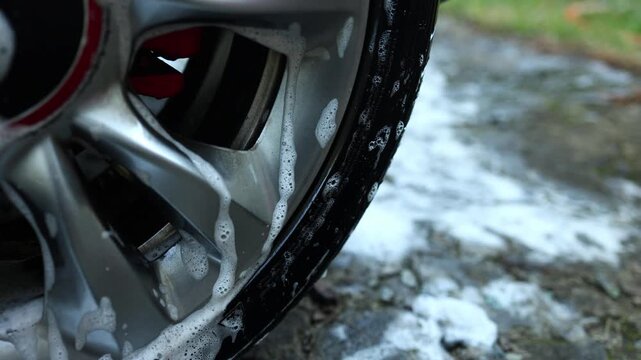 Cleaning car wheel with soap and water in a backyard during a sunny afternoon