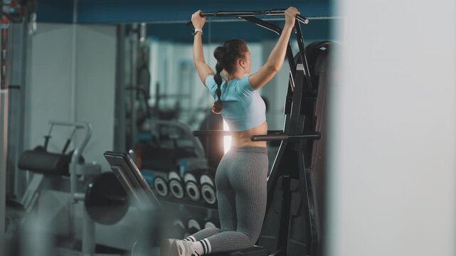Athletic woman training back muscles on pull-up machine