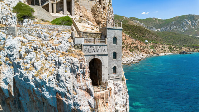 The iconic facade of Porto Flavia ore loading terminal carved into the cliffs above the turquoise waters of the Mediterranean Sea in Masua, Sardinia