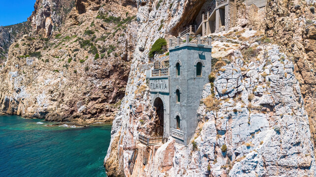 The iconic facade of Porto Flavia ore loading terminal carved into the cliffs above the turquoise waters of the Mediterranean Sea in Masua, Sardinia