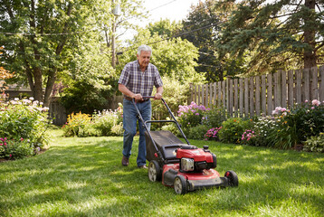 An elderly retired man mows the lawn at his country house