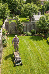An elderly retired man mows the lawn at his country house