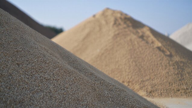 Piles of sand and gravel are stacked at a construction site under a clear blue sky. Construction materials and site preparation.