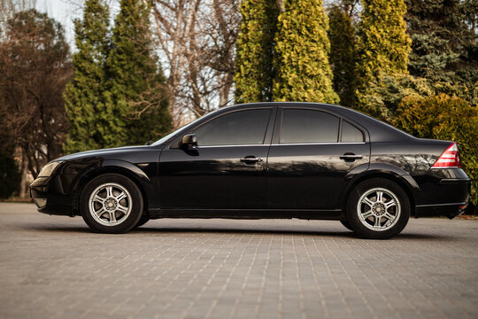 A horizontal shot of a black Ford Mondeo 2005 parked near a park