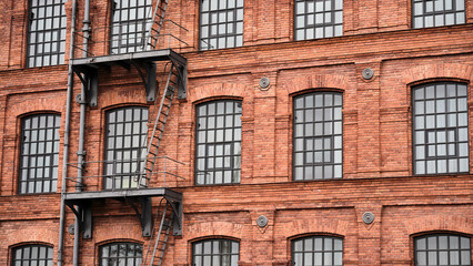 Obraz premium Industrial red brick building facade with repetitive windows, urban architecture background for design, construction and renovation concepts.