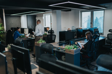 A modern open-plan office with employees at desks working on computers. A team of professionals collaborates in a contemporary workplace with plants and multiple screens.