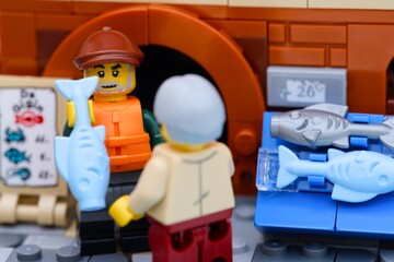 Obraz premium Tambov, Russian Federation - January 19, 2026 Close-up shot of a Lego fisherman minifigure selling a light blue fish from a fish stall to a customer.