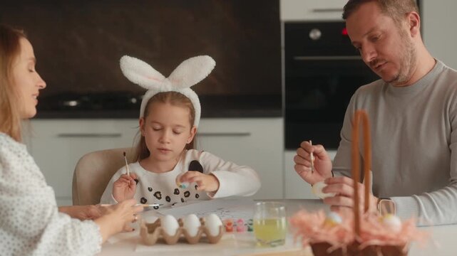 Parents and Daughter in Bunny Ears Paint Easter Eggs for the Holiday