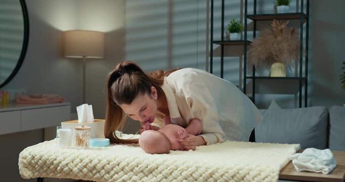 Mother gently kisses baby's feet while changing diaper on soft blanket in cozy room setting. Mother Kissing Baby's Feet