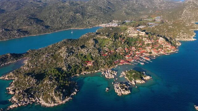 Aerial view of Kekova's sunken city, showcasing ancient amphitheater ruins amid the turquoise waters and rugged natural coastline of southern Turkey's Mediterranean region.