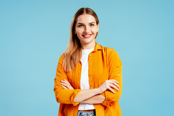 Young woman confidently smiling, arms crossed on a studio blue background