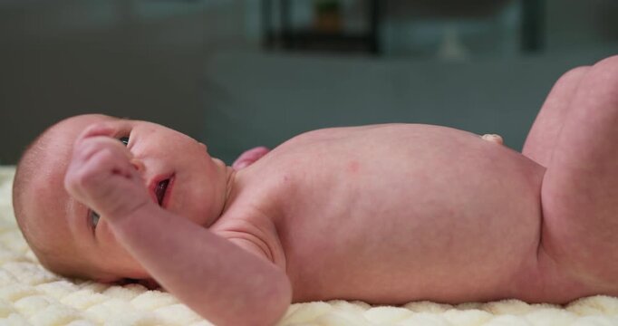 Close-up of a newborn baby's torso and face lying on a soft, textured blanket with a blurred background. Newborn Baby Lying on Blanket