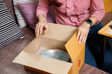 Close up of woman hands opening cardboard parcel box containing blue ceramic bowl. Customer unboxing online shopping order at home living room.