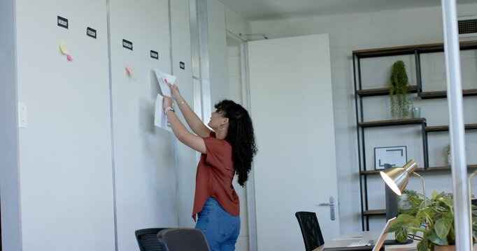 Walking with papers, hands are pinning pages onto office wall and adjusting sticky notes for plans