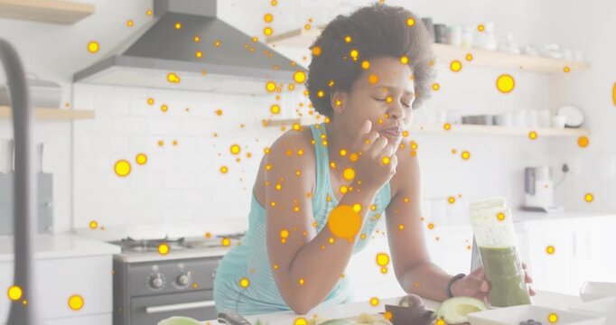 Woman bringing finger to lips tasting green smoothie, yellow dots floating over jar testing health